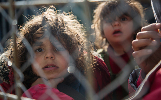 Migrant children await by the fence on the Greek side of the border to enter Macedonia near the southern Macedonian town of Gevgelija