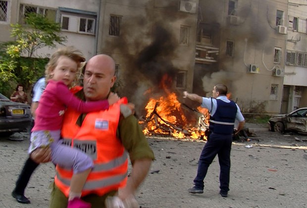 Soldado israelense retira criança de local onde houve ataque aéreo palestino nesta terça-feira (20) (Foto: AFP)